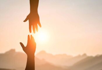 Silhouette of two people hands reaching to each other for help in sunset sky and orange sun. Friendship, teamwork, help, faith and hope concept.