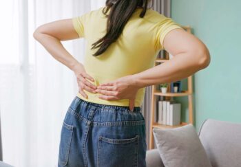 close up woman feels lower back pain in living room at home